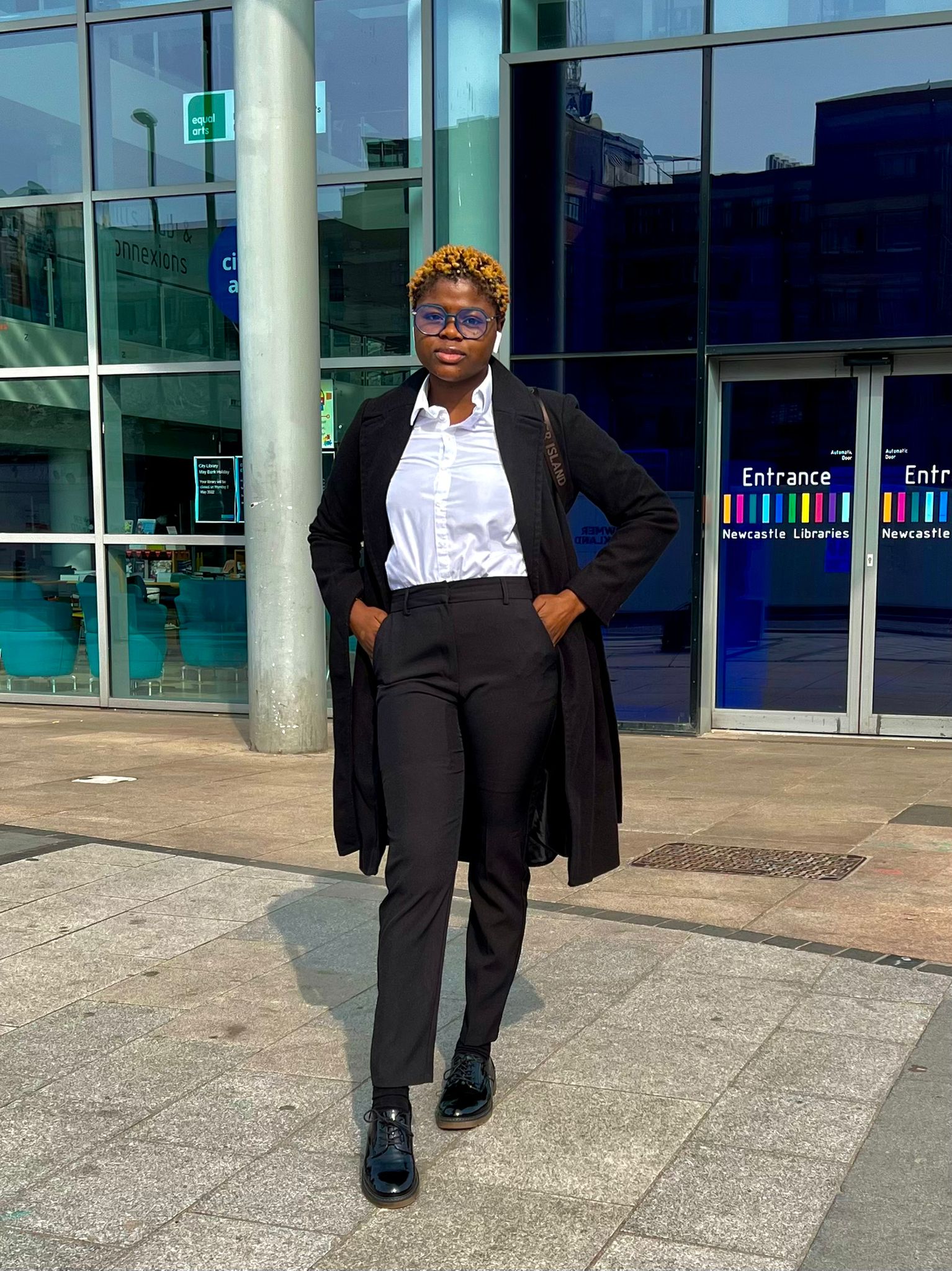 Tobiloba Olanigba or Oluwatobiloba Olanigba, standing in front of a glass building, dressed in a formal black and white clothing. Tobiloba Olanigba is a content creator, speaker, podcaster, and radio personality.