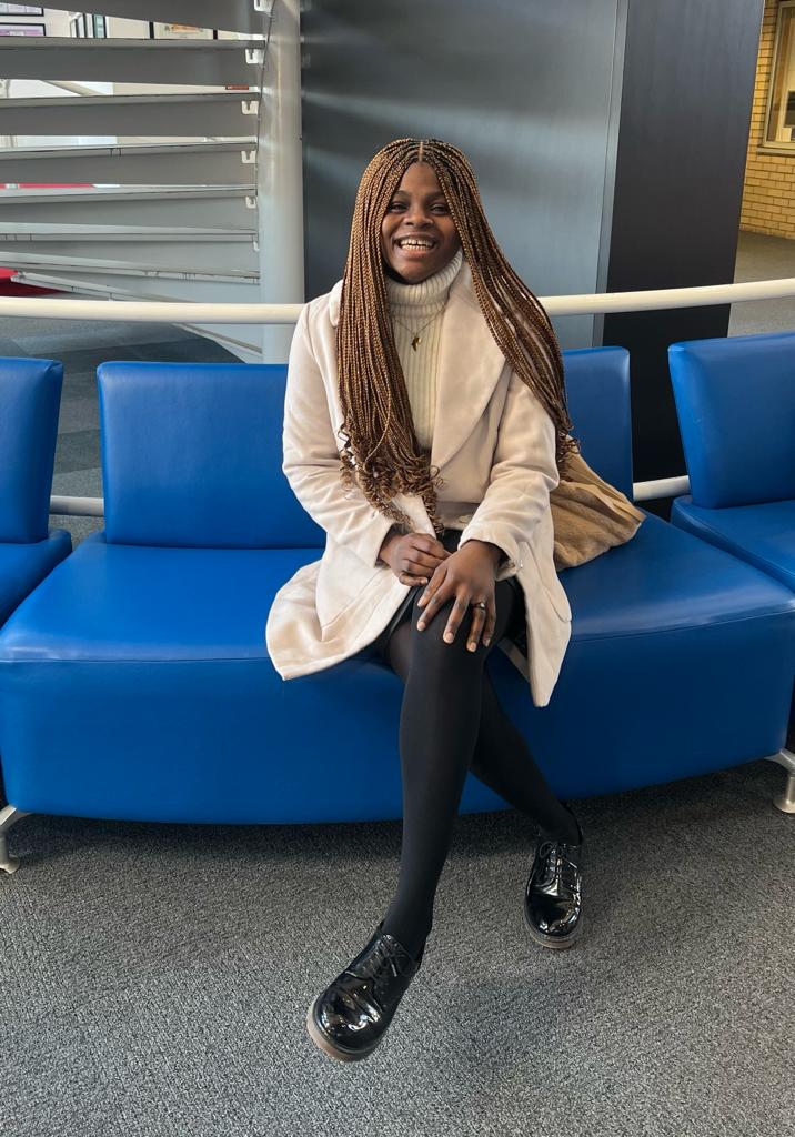 A photo of Tobiloba Olanigba also called Oluwatobiloba Olanigba, sitting on a blue couch and smiling. Tobiloba Olanigba is also known as Darling Sugar in her podcast series titled "Tell It All with Darling Sugar".