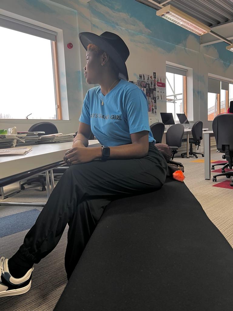 A photo of Tobiloba Olanigba or Oluwatobiloba Olanigba or Darling Sugar sitting in the office area, wearing a t-shirt and a hat. Tobiloba Olanigba is a media personality, public relations professional, and content creator.